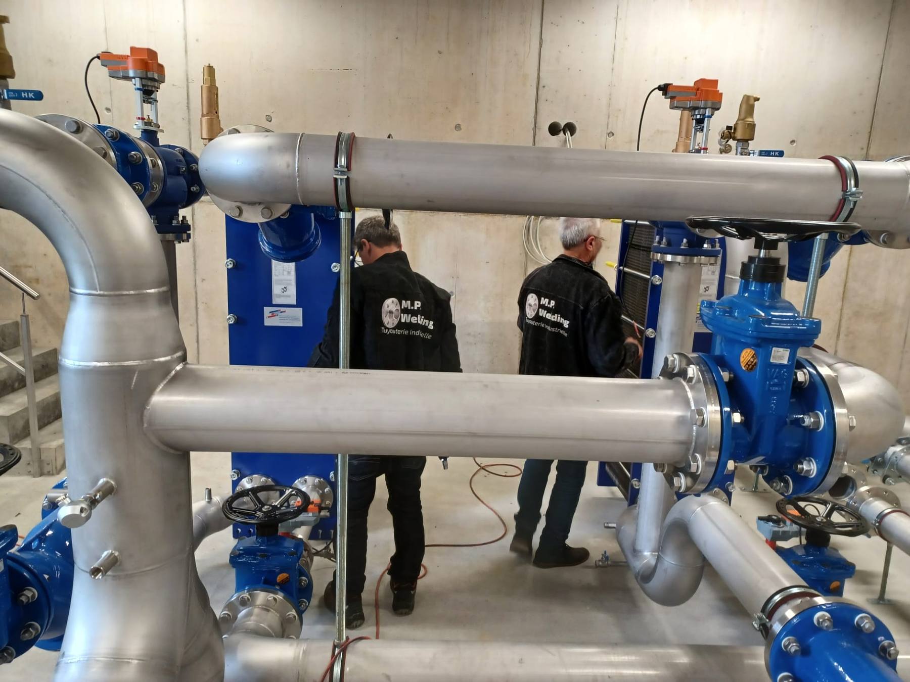 Deux techniciens devant un échangeur à plaques et des conduites inox