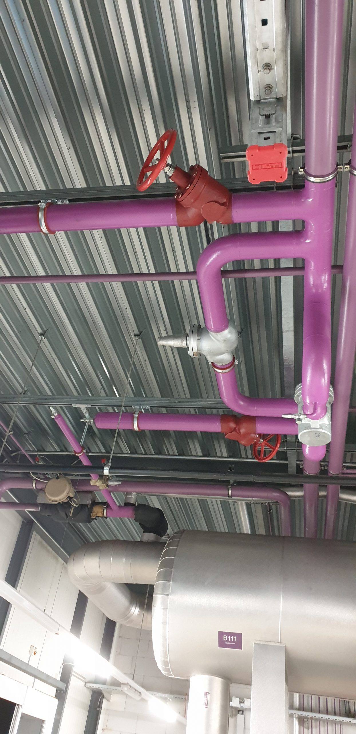 Tuyauterie colorée fixée au plafond d'un bâtiment industriel
