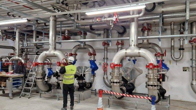 Technicien devant des collecteurs inox dans une salle technique